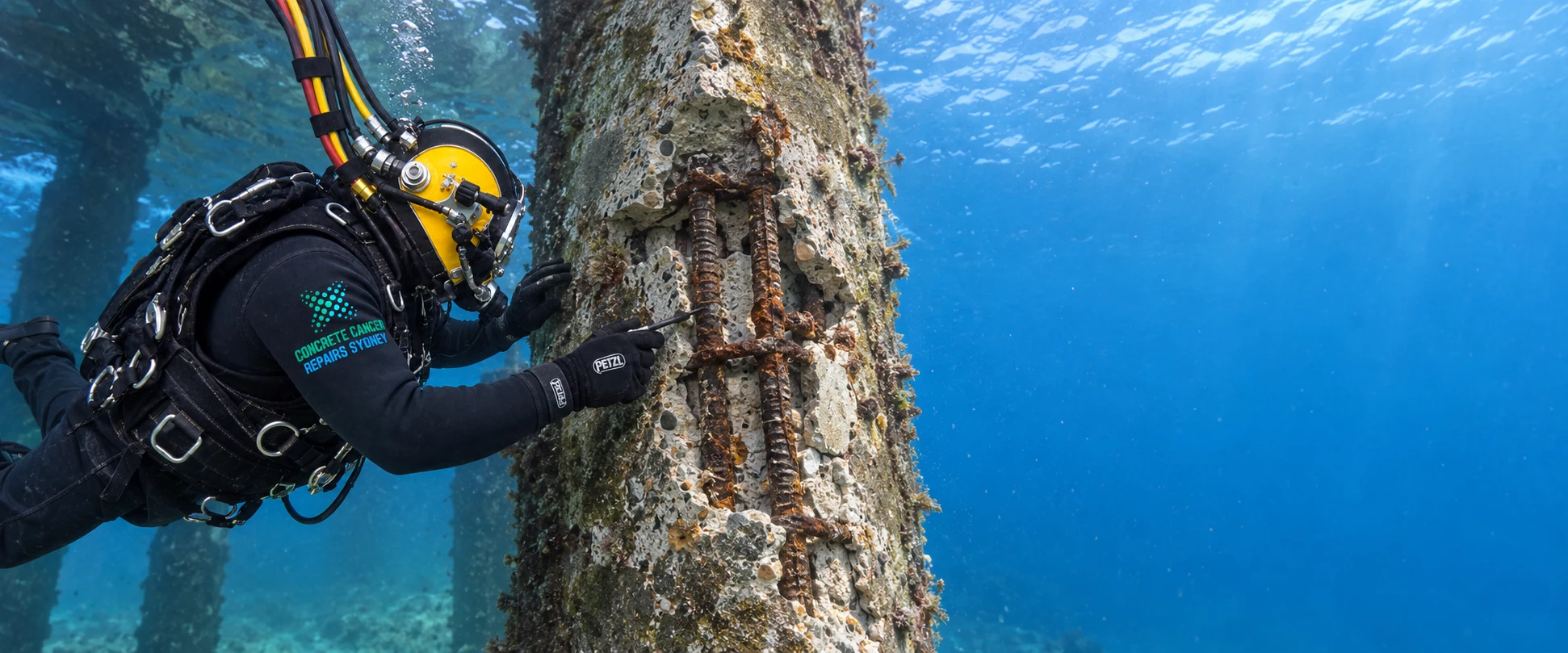 Commercial diver inspecting exposed reinforcement and concrete damage on a submerged wharf pile