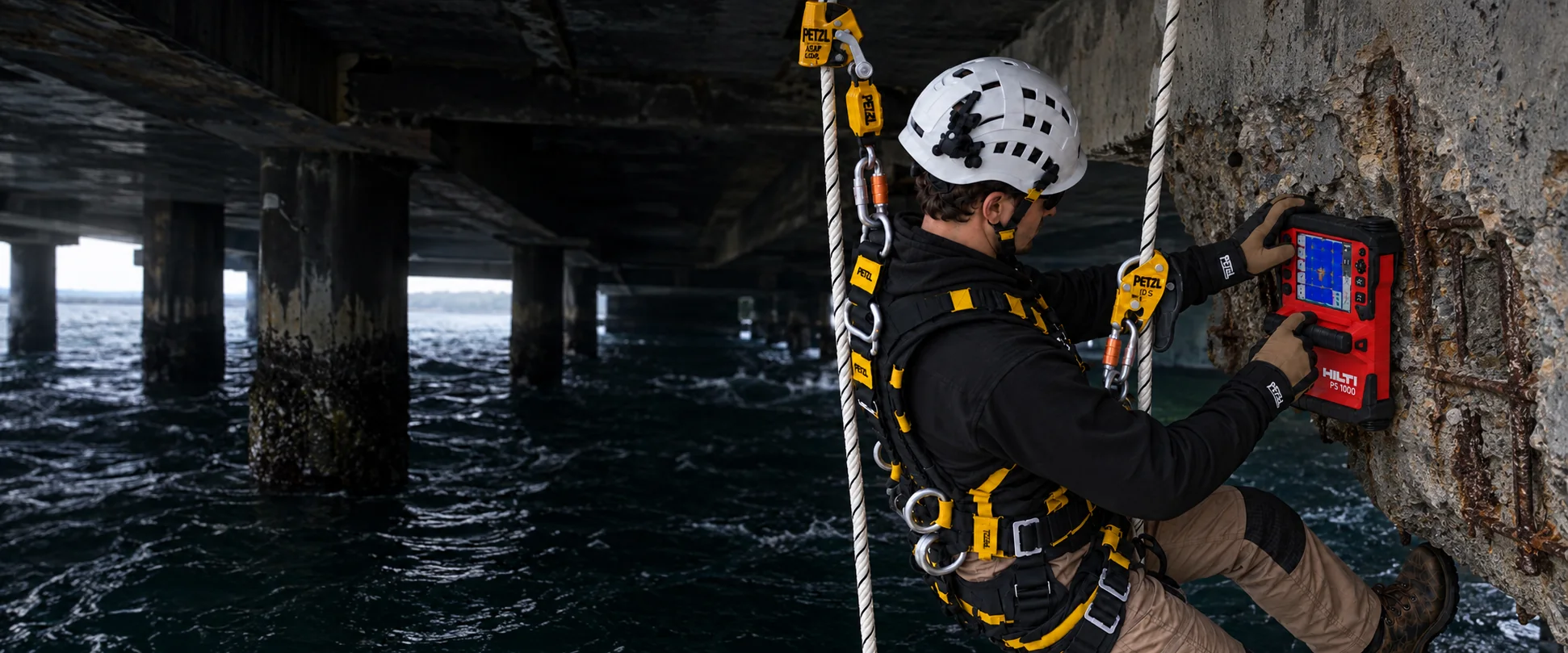 CCRS rope-access technician using a Hilti PS 1000 scanner on a deteriorated bridge pier over water