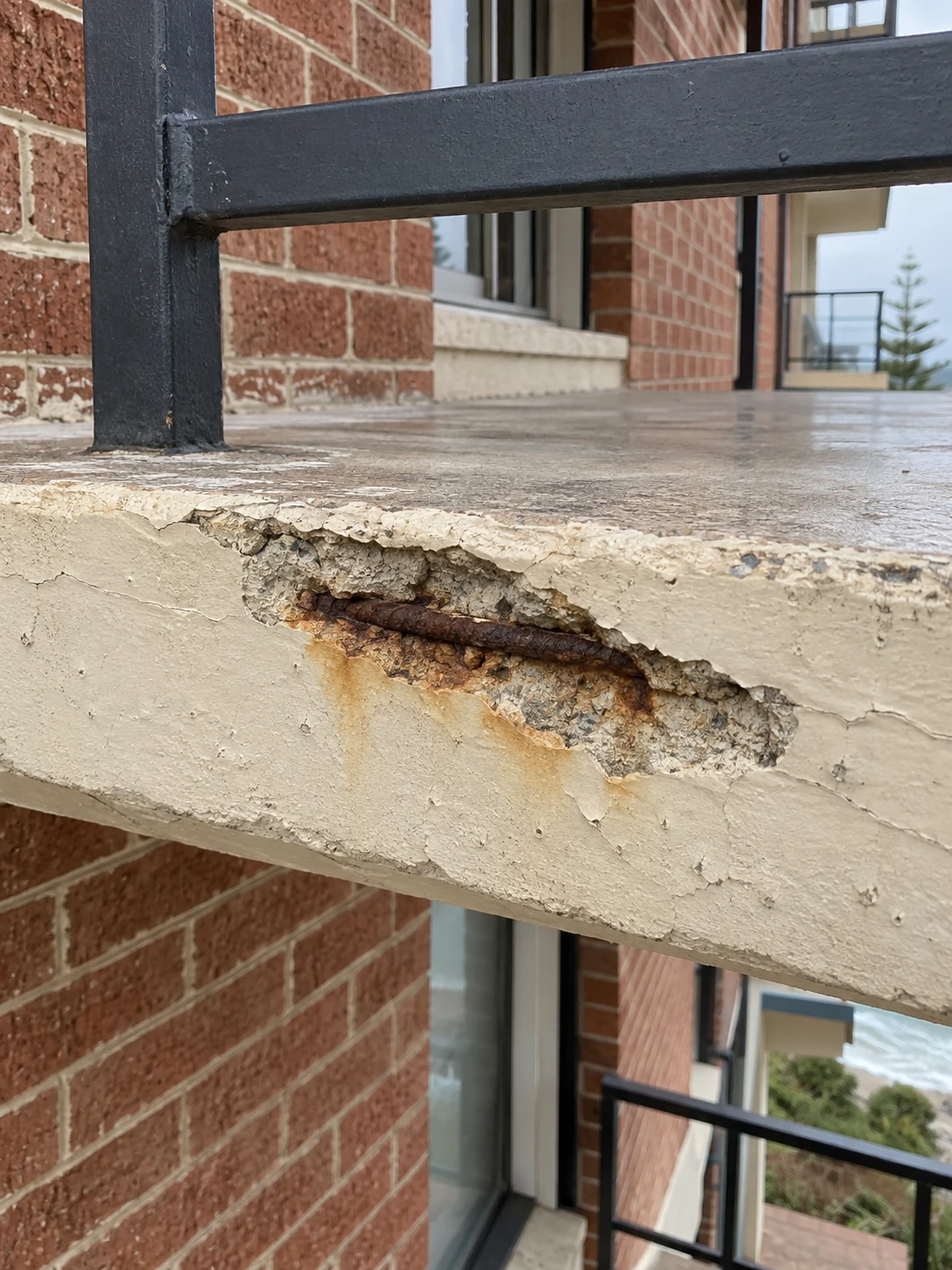 Balcony edge showing spalled concrete and exposed, rusted reinforcement.